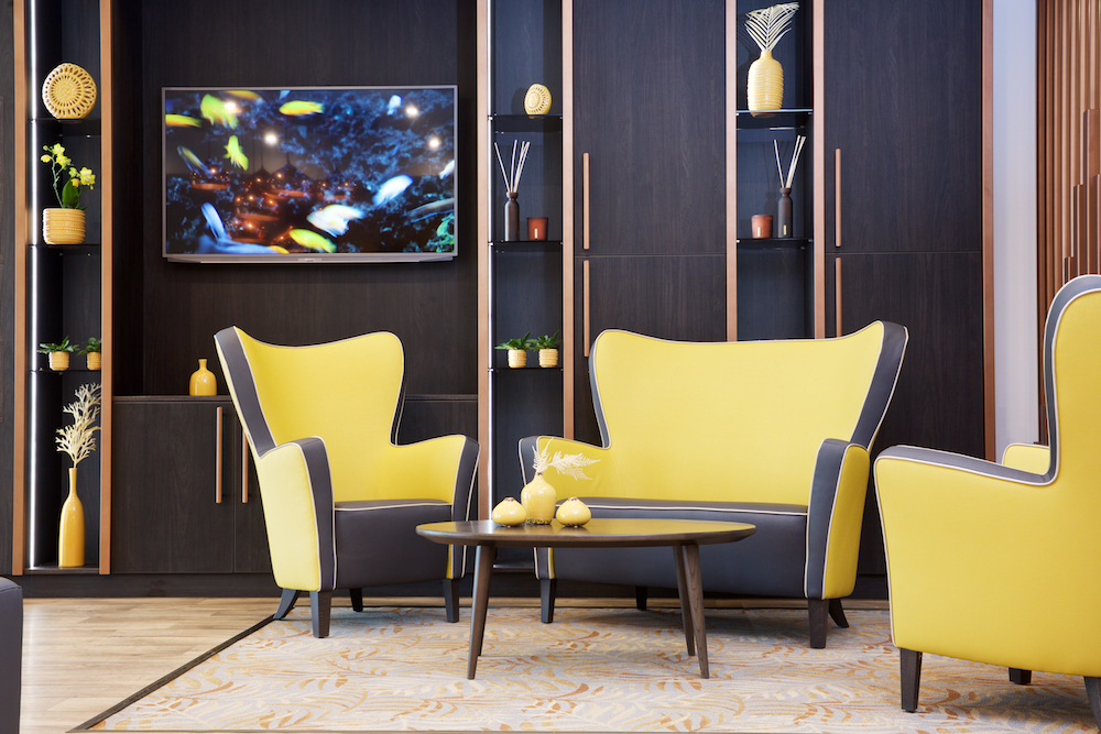 Gele fauteuils en donker houten boekenkast in een elegante ontvangstruimte, perfect voor een verzorgingshuis.