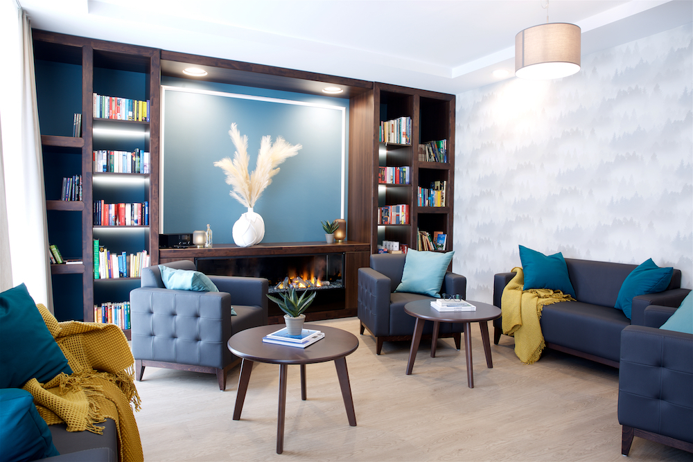 Gezellige woonkamer met een combinatie van blauwe banken en stoelen, ideaal voor het comfort van zorginstellingen en verzorgingshuizen.